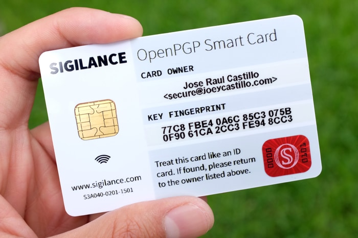 A hand holding a personalized SIGILANCE OpenPGP Smart Card, showing a printed name, email address, and key fingerprint.